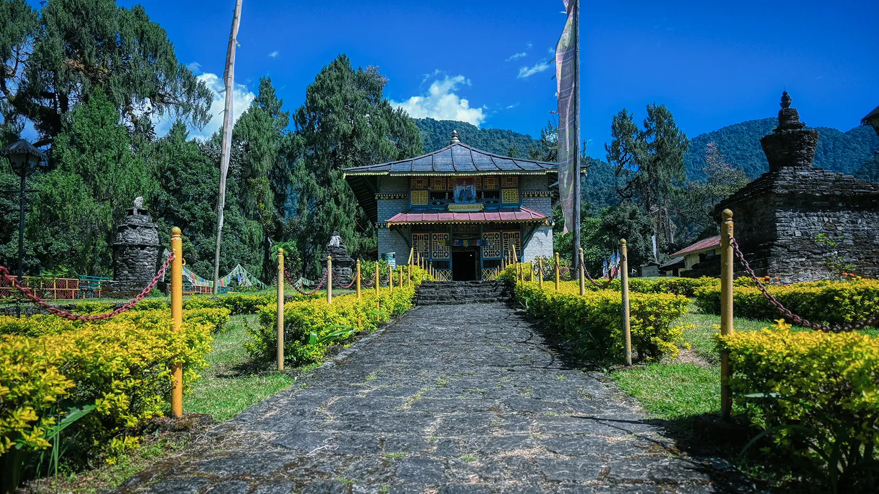 Dubdi Monastery in Yuksom, West Sikkim, showing traditional Tibetan Buddhist architecture with prayer flags and ancient stone chortens surrounded by lush gardens