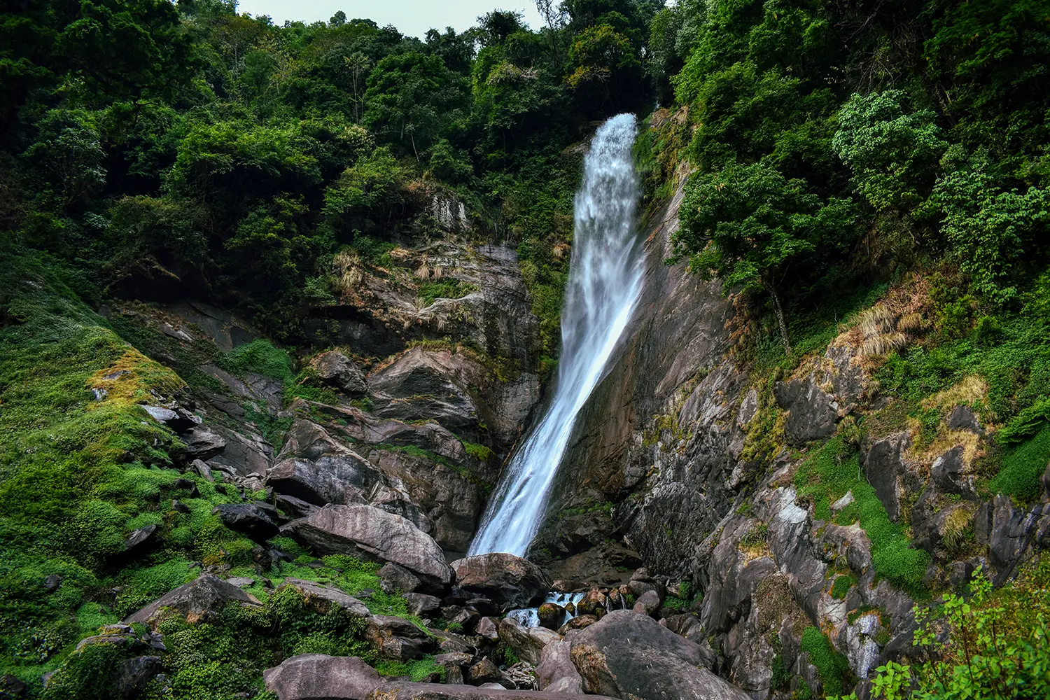 Phamrong Waterfall cascading down moss-covered rocks surrounded by lush green forest vegetation in a natural mountain setting