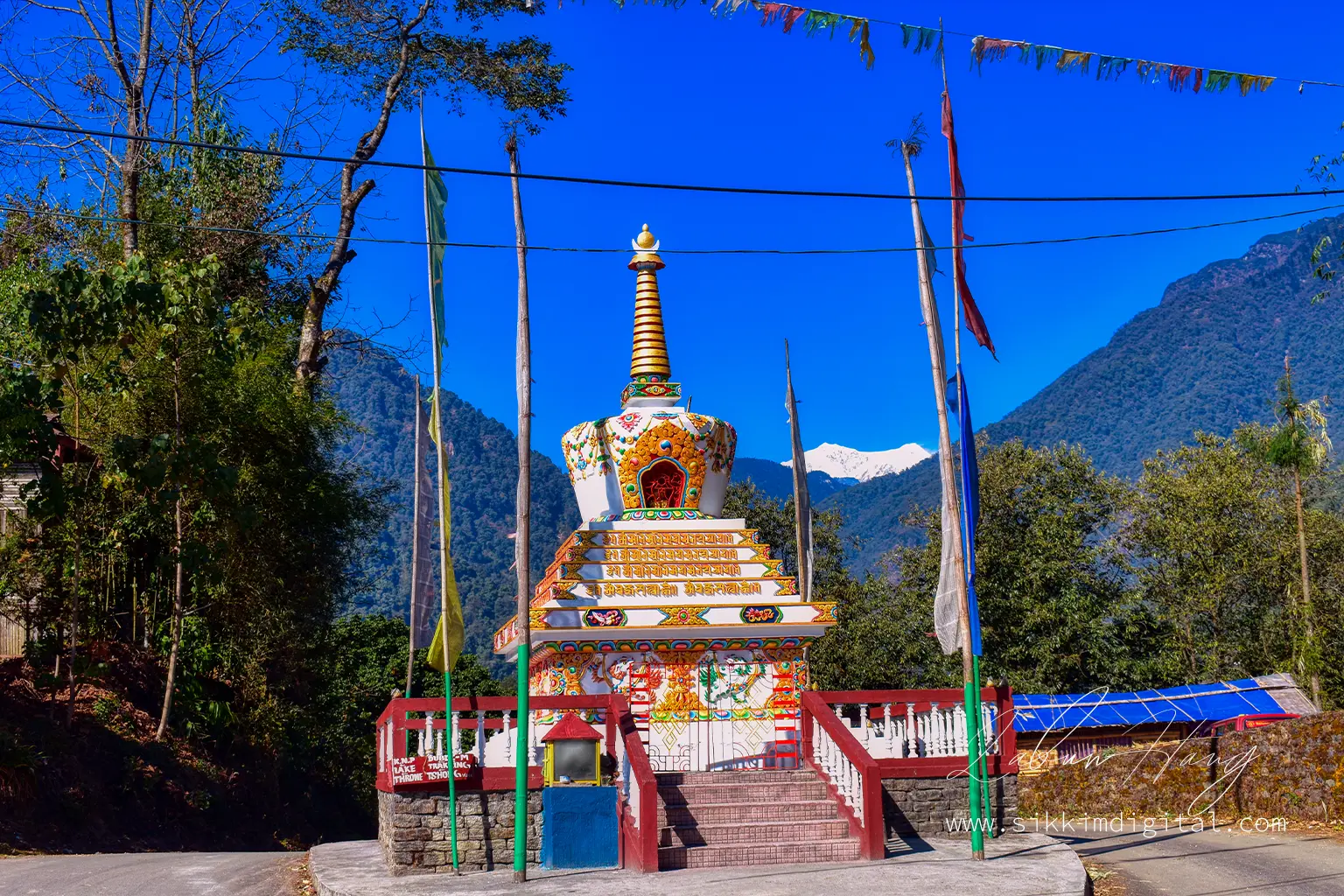Colorful Buddhist stupa in Yuksom, Sikkim, with the snow capped Kabru North and Kabru South peaks rising in the background under a vibrant blue sky.
